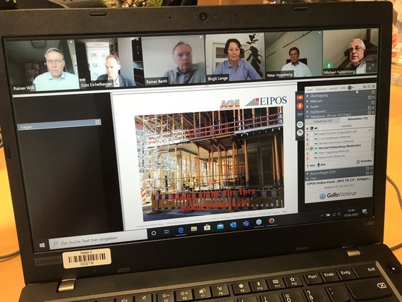 Ein Laptopbildschirm zeigt eine Video-Konferenz mit mehreren Teilnehmern und ein Baustellenaufbau im Hintergrund.