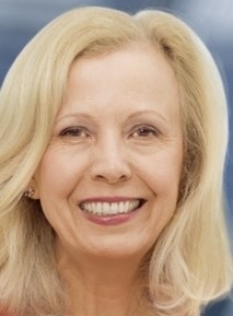 Eine Person mit blonden Haaren und einem Lächeln im Vordergrund, dunklerer Hintergrund.