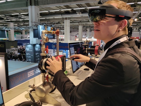 Eine Person trägt eine VR-Brille und bedient einen Roboterarm in einer Ausstellungshalle.