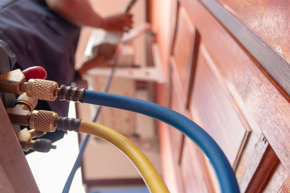 Zwei farbige Schlauchleitungen (blau und gelb) sind an einem Rohrverbinder angeschlossen, während im Hintergrund eine Person unscharf zu sehen ist.
