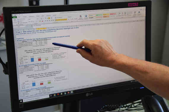 Eine Hand hält einen Stift und zeigt auf einen Computerbildschirm mit einer Benutzeroberfläche, die Text und Diagramme anzeigt.