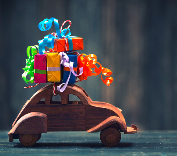 Ein hölzernes Auto trägt einen Stapel bunter Geschenke mit bunten Schleifen auf dem Dach.