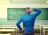 Ein Mann steht mit verschränkten Armen vor einer Tafel, auf der mathematische Gleichungen geschrieben sind.