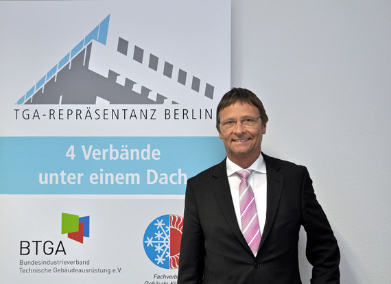 Ein Mann im Anzug steht vor einem Banner mit dem Text 