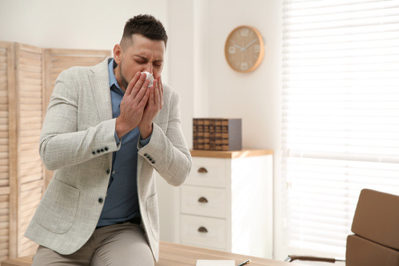 Ein Mann im Büro hält sich die Hand vor den Mund und hustet.