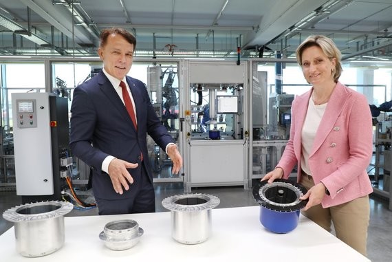 Zwei Personen, ein Mann und eine Frau, stehen in einer industriellen Umgebung und halten Metallbehälter.