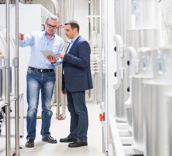 Zwei Männer stehen in einer Werkhalle und besprechen etwas auf einem Tablet.