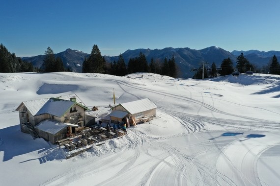 Ein Schneelandschaft mit einer kleinen Holzhütte im Vordergrund und Bergen im Hintergrund unter klarem blauem Himmel.