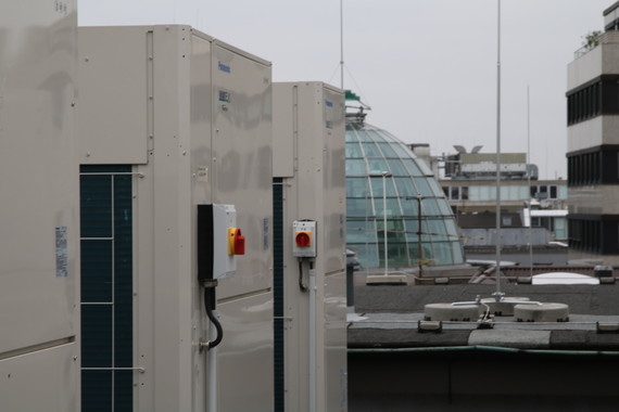 Zwei große industrielle Klimaanlagen auf einem Dach mit einem gläsernen Kuppelgebäude im Hintergrund.