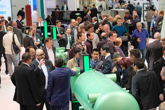 Eine Menschenmenge besichtigt eine große grüne Zylinderanlage auf einer Messe.