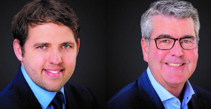 Zwei Männer in Anzügen und Krawatten lächeln in die Kamera.