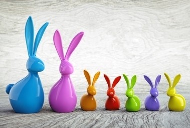 Ein Reihen von bunten Plastikhasen in verschiedenen Farben steht auf einem Holzboden.