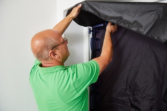 Ein Mann in einem grünen T-Shirt zieht einen schwarzen Staubmantel über einen Kühlschrank.