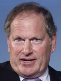 Ein Mann mittleren Alters mit blondem Haar und einem Lächeln spricht in einem Anzug und Krawatte.