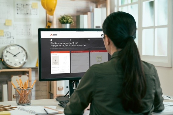 Eine Person sitzt an einem Schreibtisch und arbeitet an einem Computer, auf dem ein Dokument mit dem Titel 