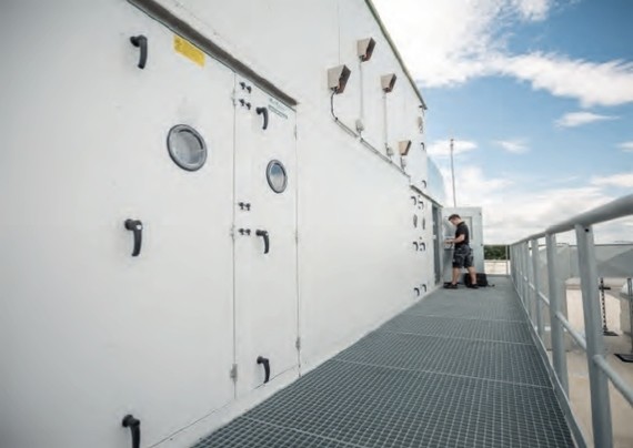 Eine weiße technische Einheit mit Metallgitterboden und Sicherheitsgeländer auf einem Dach.