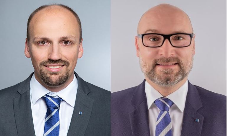 Zwei Männer in Anzügen und Krawatten, einer mit Bart und Brille, der andere mit Vollbart und Brille.