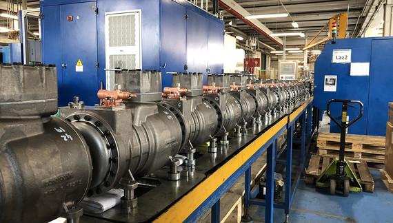 Eine industrielle Maschine mit langen, runden Rohren und blauen Metallkästen in einer Werkshalle.