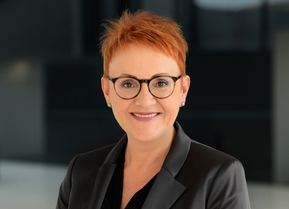 Eine Person mit kurzen, roten Haaren und einer schwarzen Jacke lächelt in die Kamera.