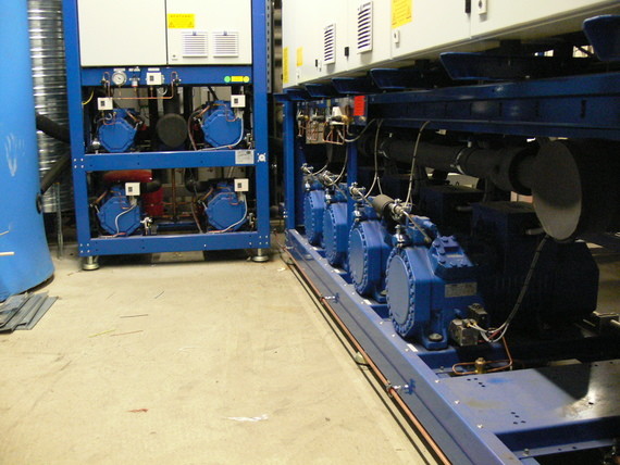 Zwei blaue industrielle Maschinen mit Rohrleitungen und Kabeln in einer Werkshalle.