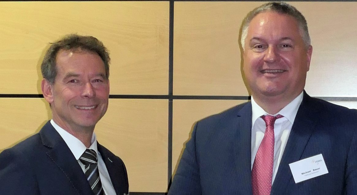 Zwei Männer in Anzügen stehen nebeneinander und lächeln in die Kamera.