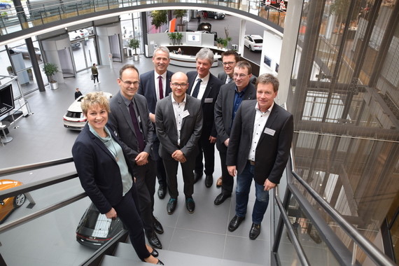 Eine Gruppe von sieben Personen in formeller Kleidung steht im Treppenhaus eines modernen Gebäudes.