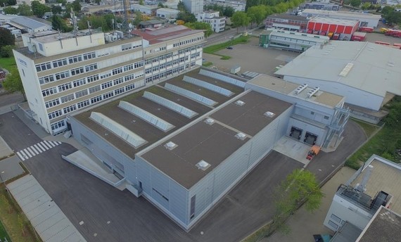 Luftaufnahme eines Industriegebäudes mit mehreren Hallen und einem großen Parkplatz.