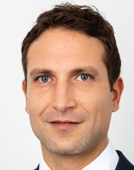 Porträt eines Mannes mit kurzen dunklen Haaren und einem hellen Hemd.