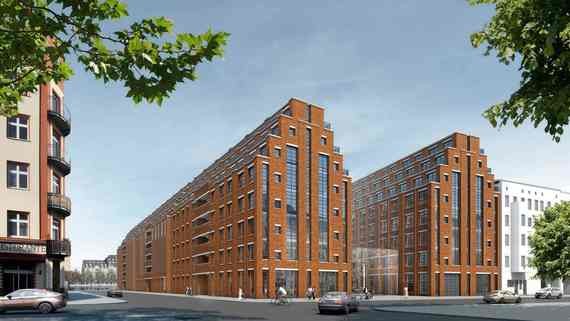 Ein modernes, mehrstöckiges Gebäude aus roten Ziegelsteinen steht an einer Straße mit Bäumen und weiteren Gebäuden im Hintergrund.