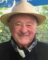 Ein älterer Mann mit weißem Haar und Bart trägt einen Strohhut und ein Hemd mit Krawatte.