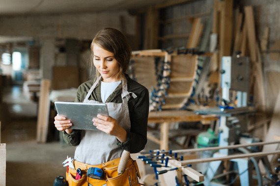 Eine Frau in einer Werkstatt hält einen Tablet-Computer und trägt eine Werkzeugweste.