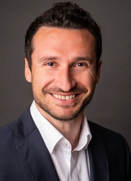 Ein Mann in einem dunklen Anzug und weißem Hemd blickt direkt in die Kamera.