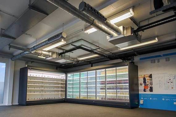 Ein leerer Raum mit Regalen, beleuchteten Vitrinen und einer blauen Informationswand.