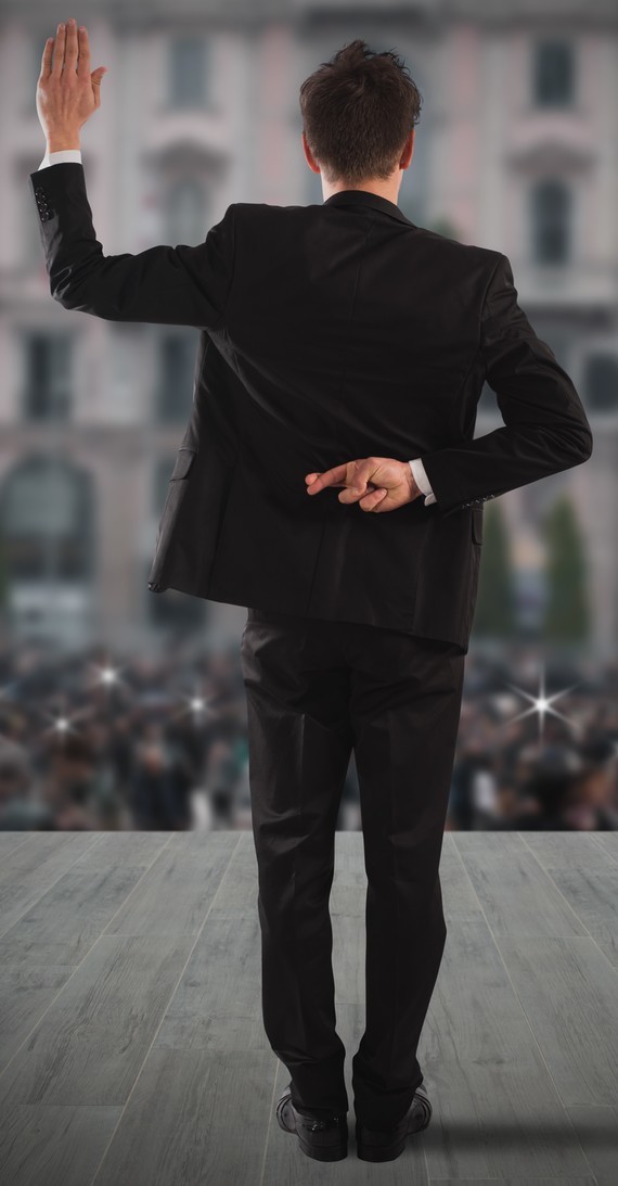 Eine Person im Anzug steht mit erhobener Hand und einer Geste, die auf eine Menge im Hintergrund zeigt.