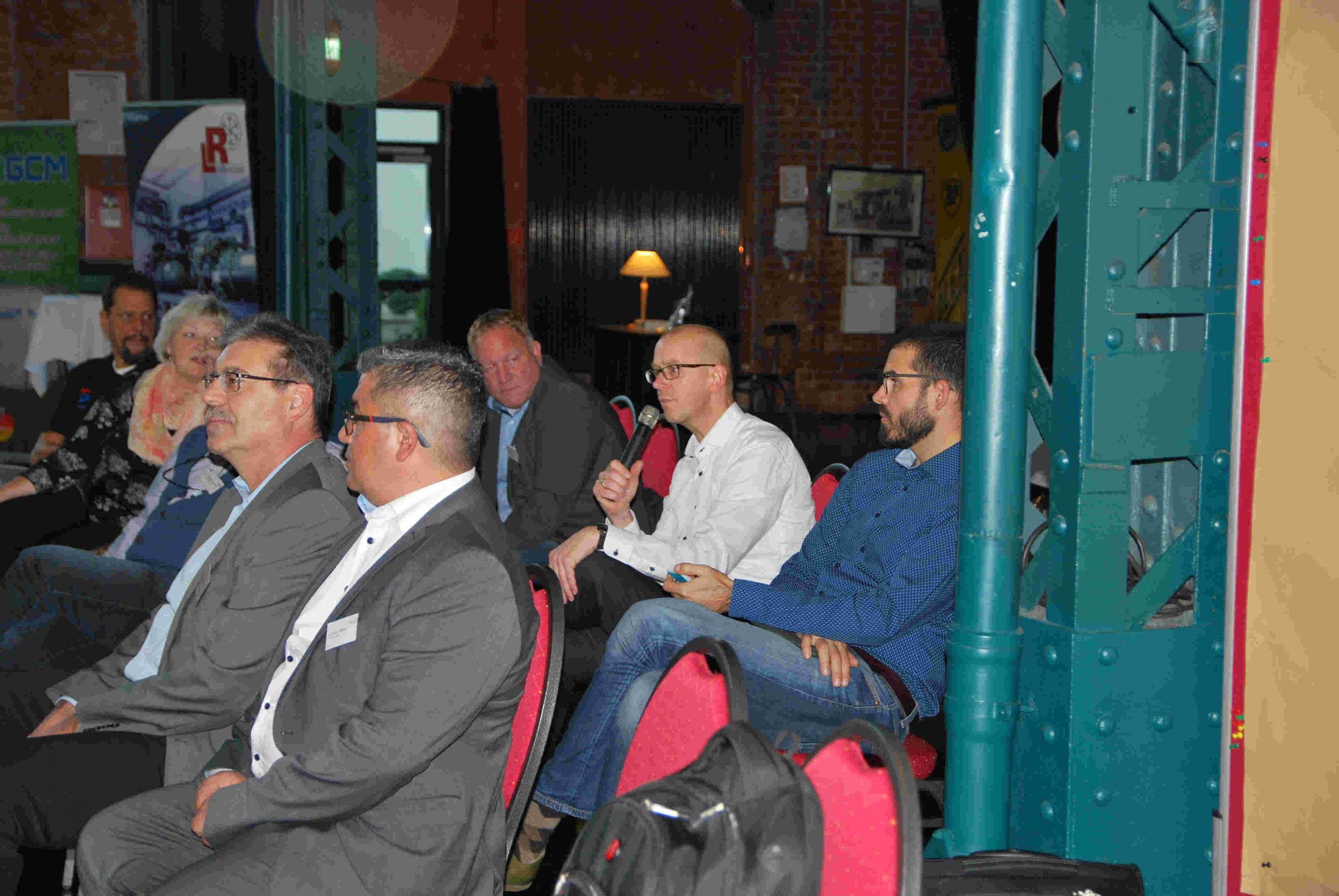 Eine Gruppe von Personen sitzt in einem Konferenzraum und diskutiert, wobei einer von ihnen ein Mikrofon hält.