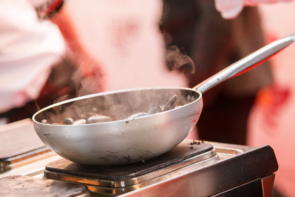 Eine Pfanne mit dampfenden Zutaten steht auf einer Kochplatte.