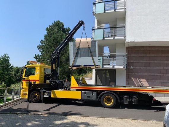 Ein gelbes und schwarzes Lastkraftwagen mit einem Kranaufbau steht auf einer Straße vor einem Wohngebäude.