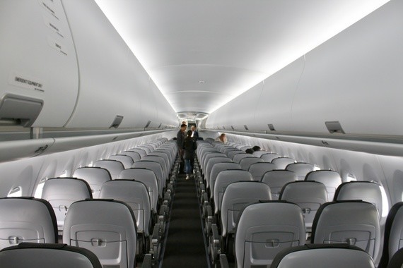 Innenraum eines Flugzeugs mit Reihen von Sitzen und einem Gang, auf dem eine Person steht.