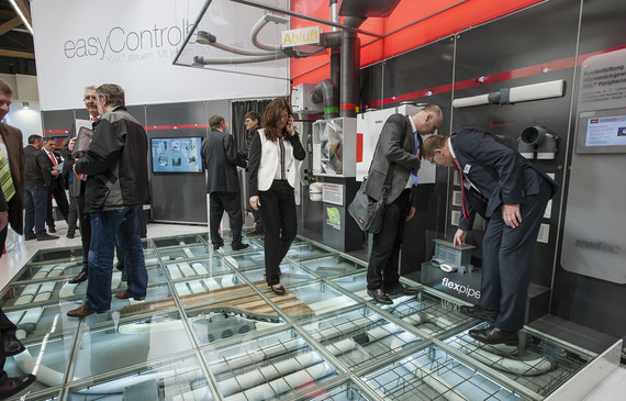 Gruppe von Menschen steht in einem modernen Ausstellungsraum und betrachtet eine interaktive Glasoberfläche.