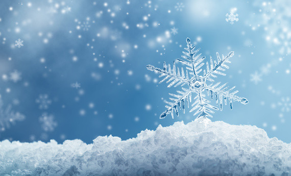 Ein großer, detaillierter Schneeflockenmuster auf schneebedecktem Boden vor einem blauen Himmel mit fallenden Schneeflocken.