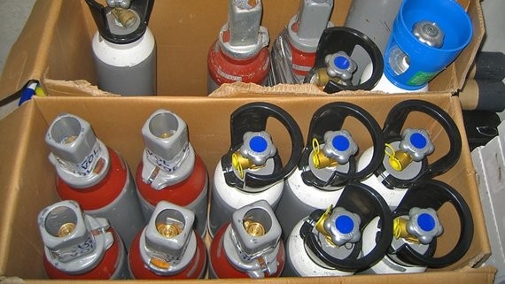 Ein Karton gefüllt mit verschiedenen Feuerlöscherflaschen in verschiedenen Farben und Größen.