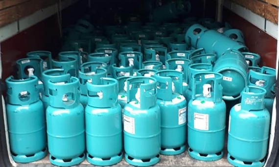 Viele blaue Gasflaschen sind in Reihen auf einem Holzboden gestapelt.