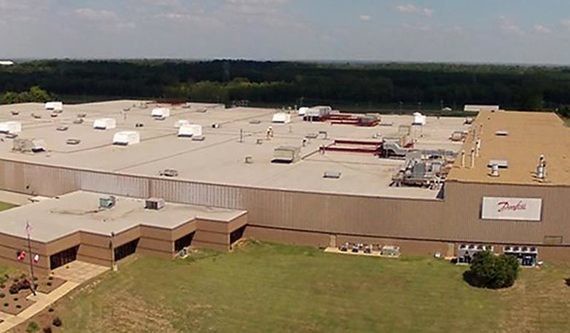 Ein Luftbild eines großen, flachen Gebäudes mit mehreren Nebengebäuden und einem Parkplatz im Hintergrund.