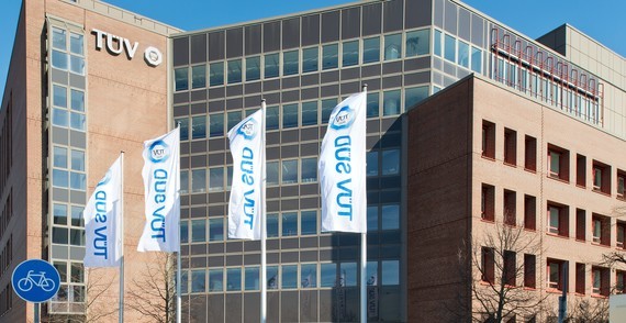 Ein modernes Bürogebäude mit mehreren hängenden Schildern und dem Logo von TÜV Rheinland.