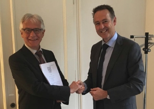 Zwei Männer in Anzügen schütteln sich die Hände, während einer von ihnen ein Dokument hält.