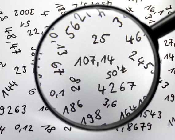 Eine Lupe vergrößert Zahlen und mathematische Formeln auf einem Papier.