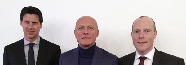 Drei Männer in Anzügen stehen nebeneinander vor einem weißen Hintergrund.