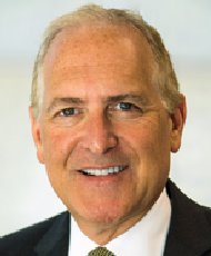 Ein Mann mit grauem Haar und Bart, der lächelt und ein Hemd mit Krawatte trägt.