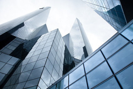 Ein Bild von mehreren glänzenden, spiegelnden Hochhäusern mit einem Blick nach oben unter einem bewölkten Himmel.