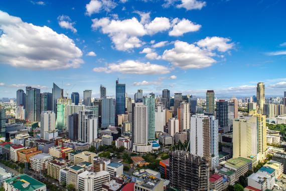 Eine Luftaufnahme einer städtischen Skyline mit hohen Wolkenkratzern und niedrigeren Gebäuden unter einem blauen Himmel mit weißen Wolken.